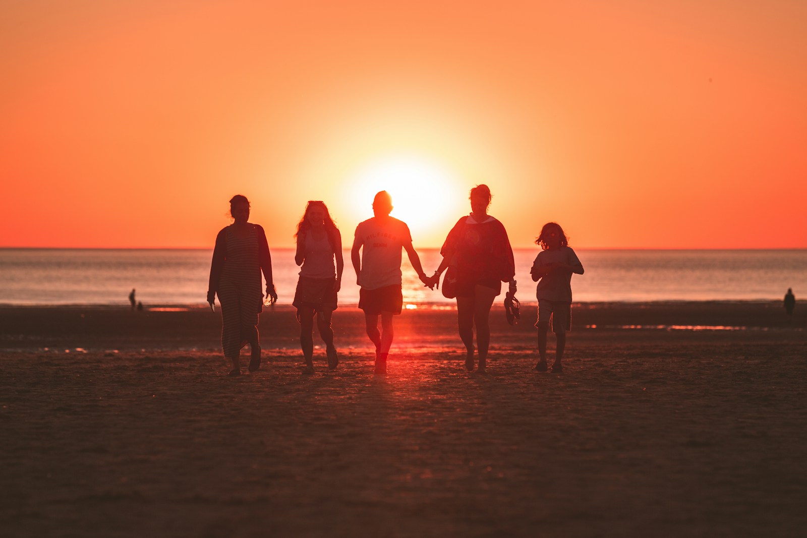 Silhouette of a family of five walking on the beach at golden hour, viewed from behind
